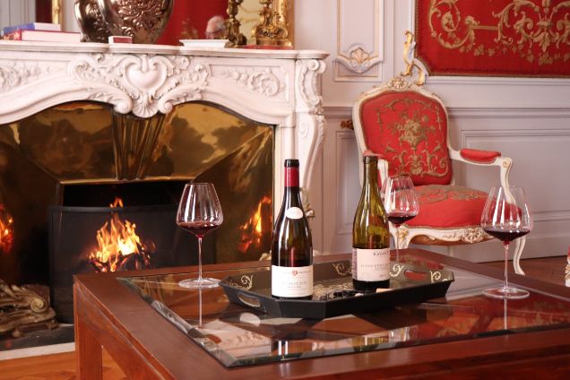 A luxury private wine tasting setup in a historic French manor with a fireplace, featuring bottles of Échezeaux Grand Cru and professional glassware.
