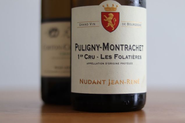 A bottle of Puligny-Montrachet 1er Cru Les Folatières by Jean-René Nudant, a highlight of bespoke white wine tastings in Burgundy.